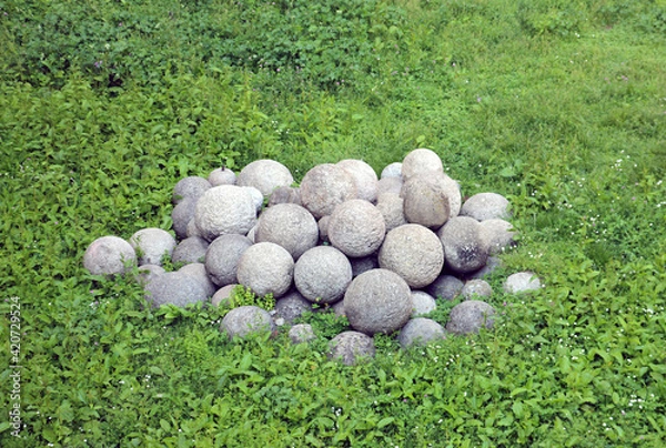 Obraz pile of ancient medieval round stone granite cannonballs lie in the green grass