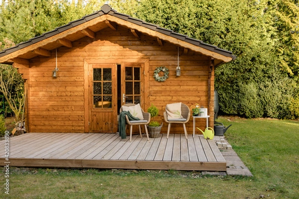 Fototapeta Nice wooden hut in a green garden. Garden shed with chairs and flowers. Spring mood. Drinking tea outside in spring. 