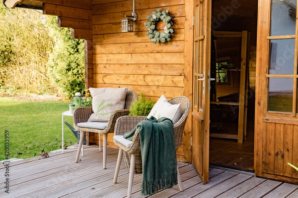 Fototapeta Nice wooden hut in a green garden. Garden shed with chairs and flowers. Spring mood. Drinking tea outside in spring. 