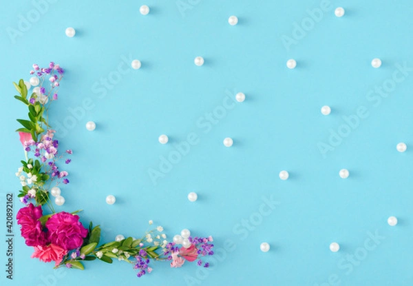 Fototapeta Creative and unique spring concept made with flowers, leaves and white pearls on pastel blue background. Beautiful and elegant idea for wallpaper. Minimal flat lay.