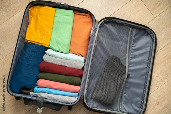 Fototapeta Top view of an open suitcase prepared for travel. Neatly folded clothing for the vacation trip. Excited state before the trip.