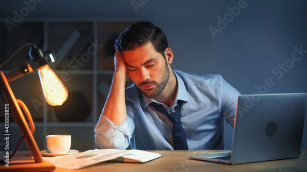 Fototapeta sleepy man with closed eyes working late in office
