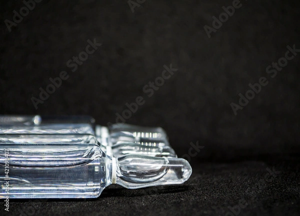 Fototapeta Glass medical ampoule vial for injection. Medicine is liquid sodium chloride with of aqueous solution in ampulla. Close up. Bottles ampule multicolor on background color and water. Human plasma.