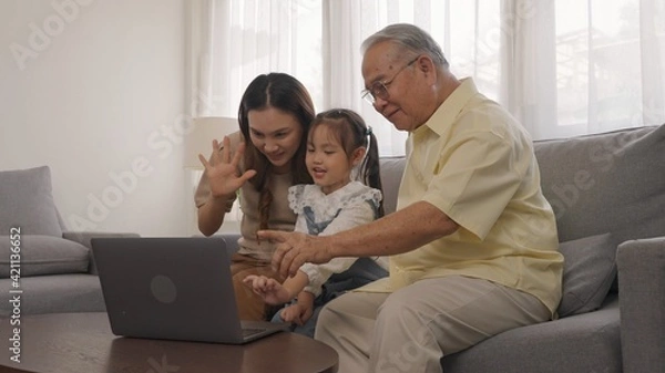 Obraz Shot of happy family: grandfather, daughter and granddaughter having fun to make selfie or video technology call to family and relatives with tablet or laptop on sofa in living room.