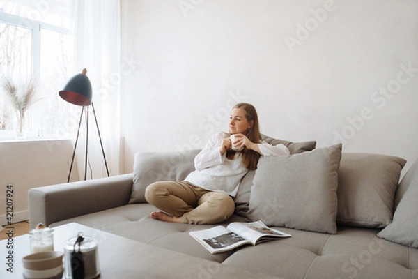 Fototapeta Young woman relaxing on the couch with hot beverage at home.
