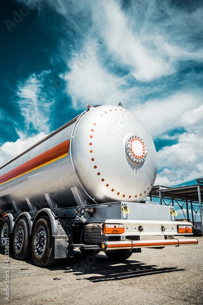 Fototapeta Truck with trailer, tank with flammable liquid, sunny day outside, metallic color container, blue sky with white clouds, gravel