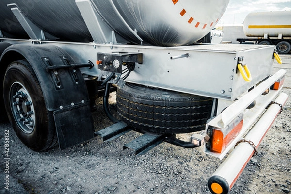 Fototapeta Truck with trailer, tank with flammable liquid, sunny day outside, metallic color container, blue sky with white clouds, gravel