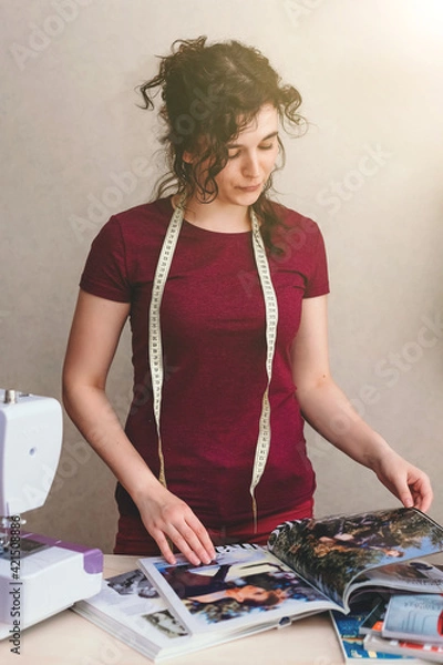 Obraz Happy attractive young woman seamstress sitting and sews on sewing machine in studio