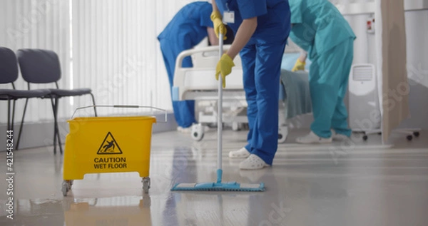 Fototapeta Nurses mopping floor and making bed in empty hospital ward