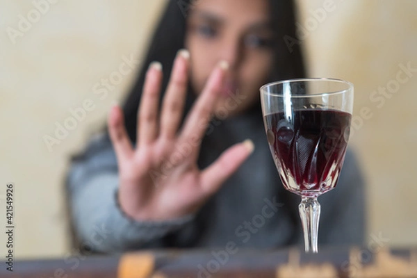Obraz Giving up alcohol. A young woman at the table refuses with her hand a glass of red wine. Selective focus