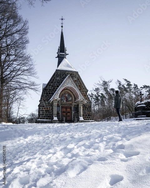 Fototapeta man standing in front of a chapel in the snow