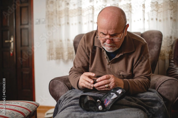 Fototapeta Senior men with glucometer checking blood sugar level at home