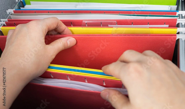 Fototapeta Closeup person's hand pick red hanging file folder from drawer.  Administration clerk finding paperwork from office storage. Corporate information record organization and database management concept.