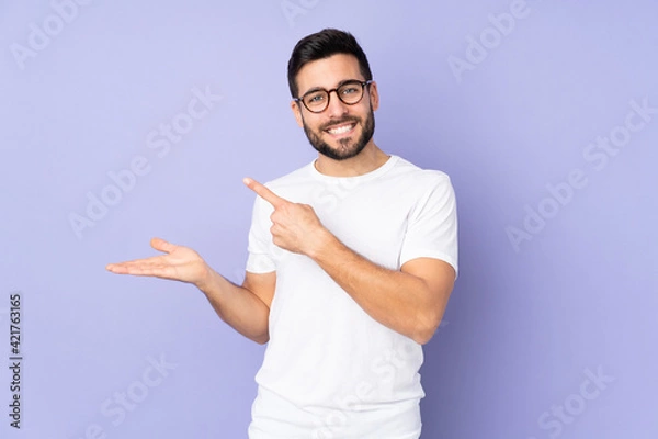 Fototapeta Caucasian handsome man over isolated background holding copyspace imaginary on the palm to insert an ad