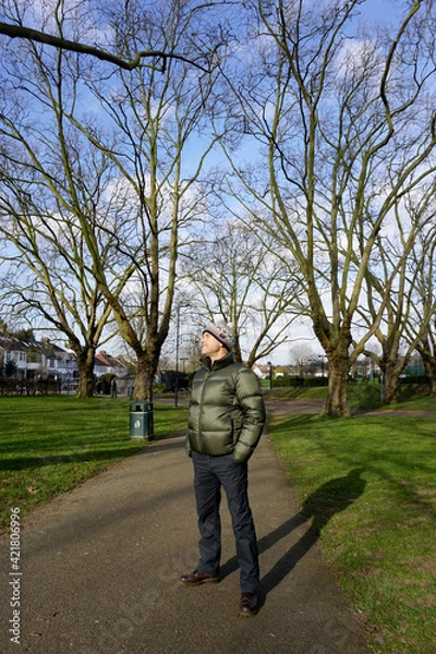 Fototapeta Portrait full body of handsome Caucasian man  wearing green jacket, bobble hat with white pom pom stand looking up the blue sky in the park 