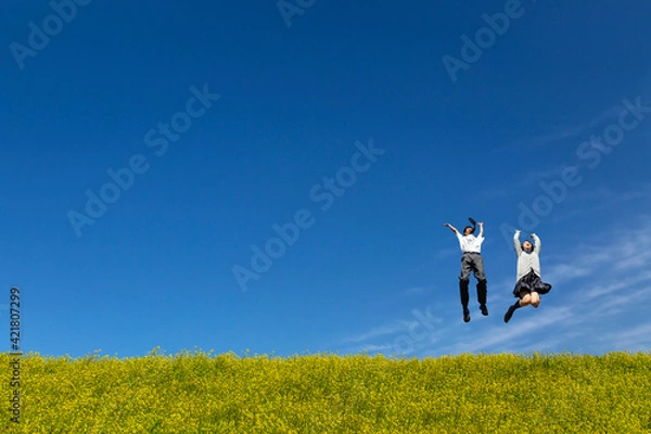 Obraz 菜の花の咲く土手でジャンプをする男女の高校生。春、入学、お祝い,卒業,合格イメージ