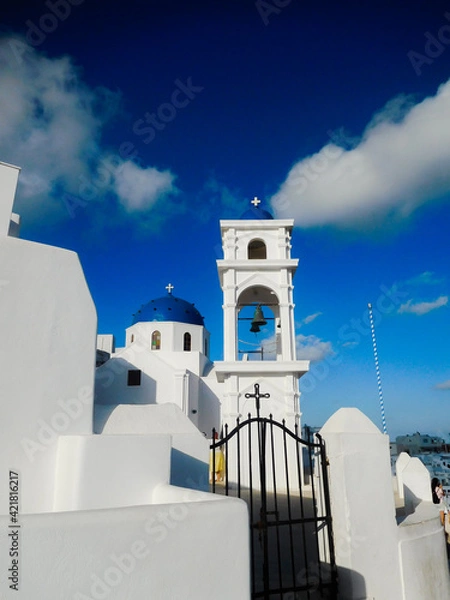 Fototapeta Whitewashed walls, tower and blue dome of one of the many churches on Santorini