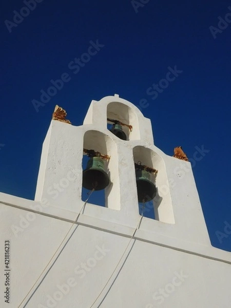 Fototapeta Whitewashed walls, tower and blue dome of one of the many churches on Santorini