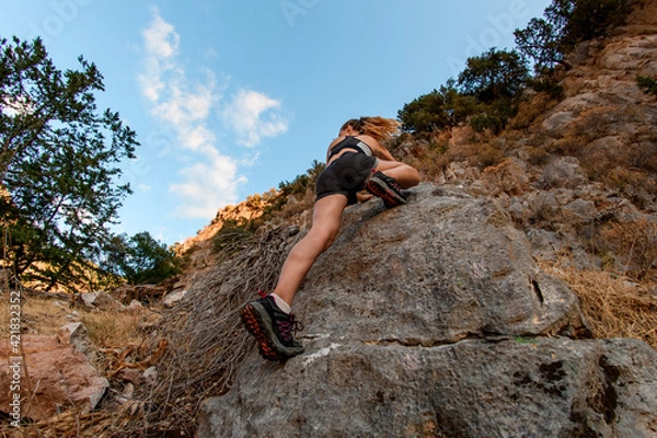 Fototapeta bottom view of sportive woman who climbing up on rocks using rope.