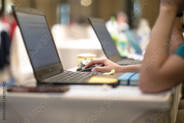 Fototapeta Action of a business person is typing on keyboard to make a report, with blurred background of bokeh lighting in business conference meeting. Close-up and selective at person hand.