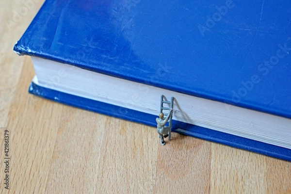 Fototapeta Miniature figurine character: one man stepping on the ladders to get on blue book, make the effort, study concept
