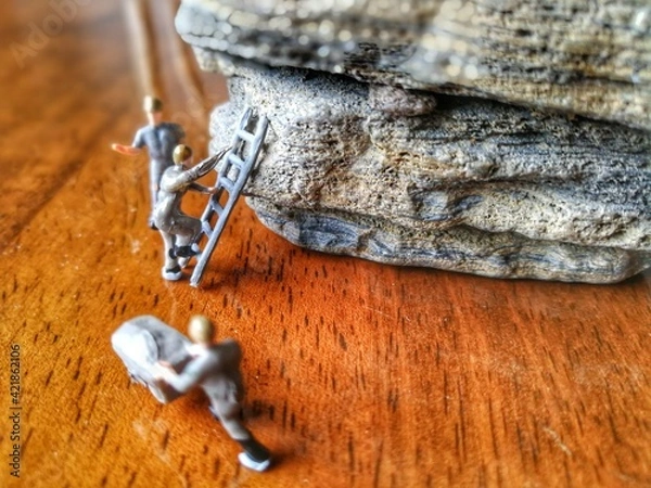 Fototapeta Miniature figurine character as engineering working on rock mountain with ladders, cart. They are set on wooden floor