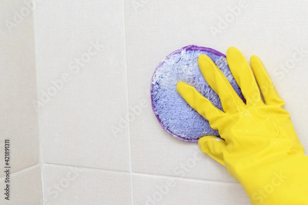 Obraz A woman's hand in a yellow glove cleans the tiles in the bathroom with detergent.Cleaning the house.Cleaning of dirty plaque
