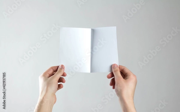 Fototapeta Hands holding a white folding flyer. A clean flyer in your hands. For your text. Isolated on a gray background