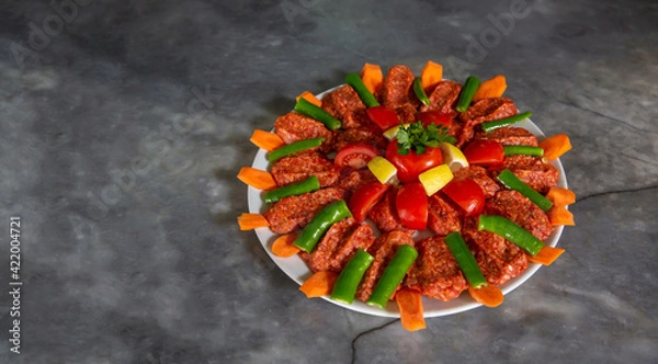 Fototapeta top view, Turkish food uncooked meatballs in round plate, on marble background. Serving plate garnished with tomatoes, carrots and green peppers.