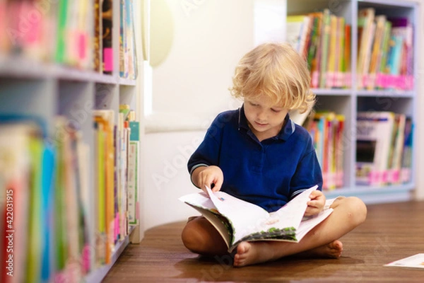 Fototapeta Child in school library. Kids reading books.