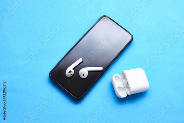 Fototapeta White wireless bluetooth earphones or headphones, plastic case or box for storage and charging and smartphone, on color background close up
