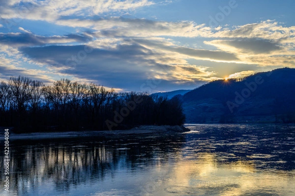 Fototapeta The sun disappearing behind the hills reflecting in the Danube river in Austria