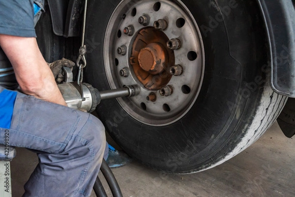 Fototapeta Tire workshop operator removing the lug nuts from a truck wheel with a pneumatic machine.