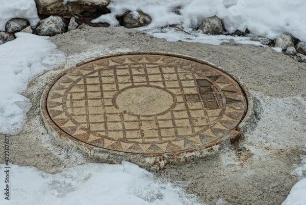 Fototapeta one rusty iron manhole on gray concrete in a snowdrift of white snow 