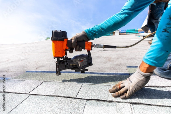 Obraz roofer installing roof shingles with nail gun