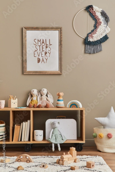 Fototapeta Stylish scandinavian newborn baby room with brown wooden mock up poster frame, toys, plush animal and child accessories. Cozy decoration and hanging cotton flags on the beige wall. Template.