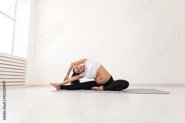 Fototapeta Purposeful pregnant woman exercises during yoga class and relaxes while sitting on a mat on the floor. Concept of physical and mental preparation of the body for childbirth. Place for text