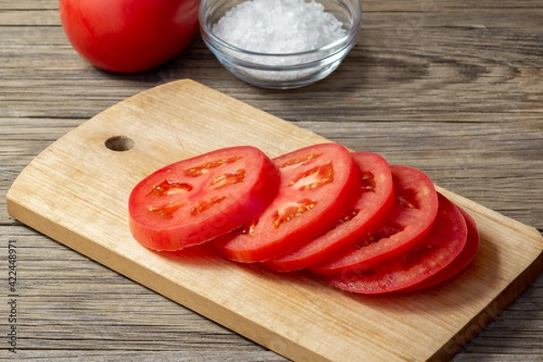 Fototapeta Tomato sliced into round slices on a wooden cutting board