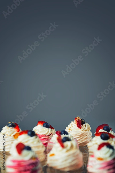 Fototapeta Close up of mini Pavlova cakes. Meringue with cream topping and fruit. Composition with blank space for a text.