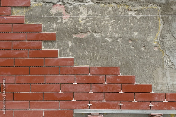 Fototapeta Wall or fence decoration. Laying decorative tiles for red bricks on a vertical surface
