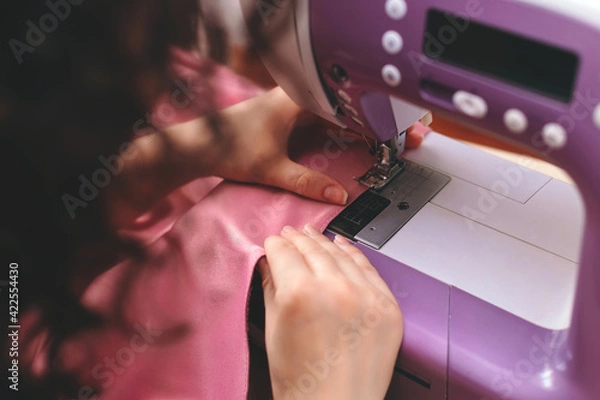 Obraz Happy attractive young woman seamstress sitting and sews on sewing machine in studio