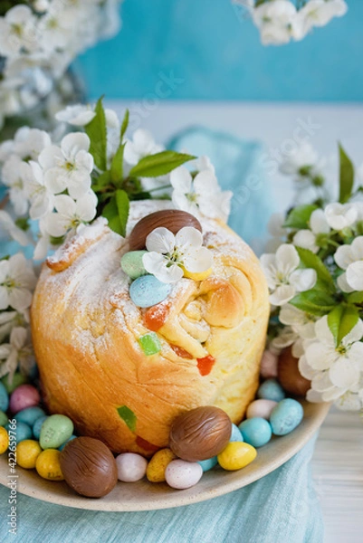 Fototapeta Traditional cupcake Easter cake kraffin with raisins on blue background. Cherry blossom, choco eggs. Close up of homemade cake. Cruffin with candied fruits. Food. Copy space.