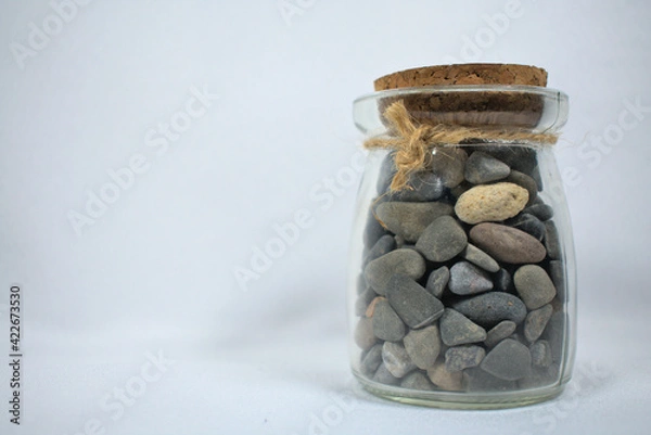 Fototapeta Glass jar filled with stones closed with cork and string on white background