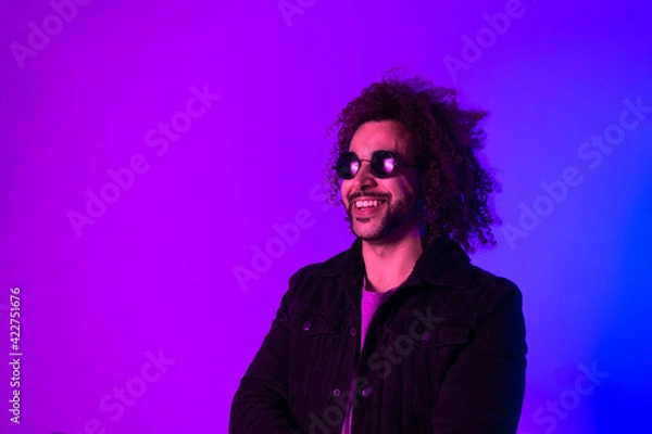 Obraz Portrait of an Afro-American hipster man, afro hair, in the style of the 80s and 90s, steampunk glasses, blue and purple neon lights. smiling and laughing