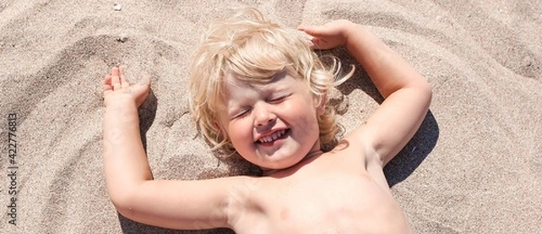 Obraz Little boy lying on the sand and playing on the beach of Mediterranean sea. Summertime, vacation, travel banner.	