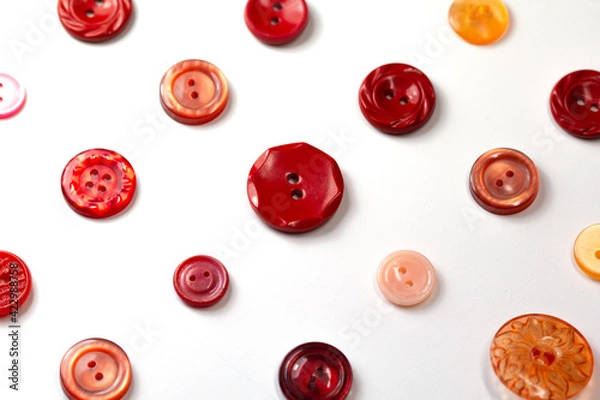 Fototapeta Colorful red and pink buttons on a white background. Set of red buttons. Old vintage buttons close up. Copy space. Top view. Background of buttons.
