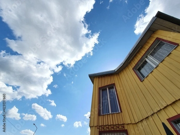 Obraz A building with yellow walls against a clear sky. Small windows look out onto the street, offering a view of the clear sun.