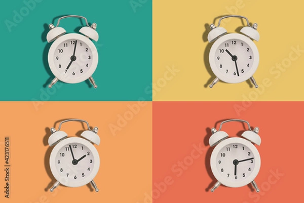Fototapeta Four alarm clocks on a colored background. The hands of the clock show different times. Flat lay