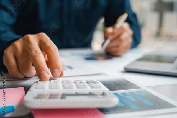 Fototapeta Male accountants or businessmen use a calculator and laptop to calculate investment results. And making financial reports on the desk Business finance accounting concept