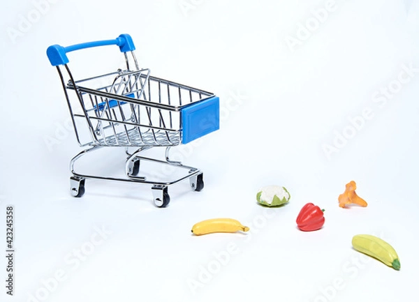 Fototapeta A blue supermarket grocery cart on an isolated white background with scattered fruits and vegetables.